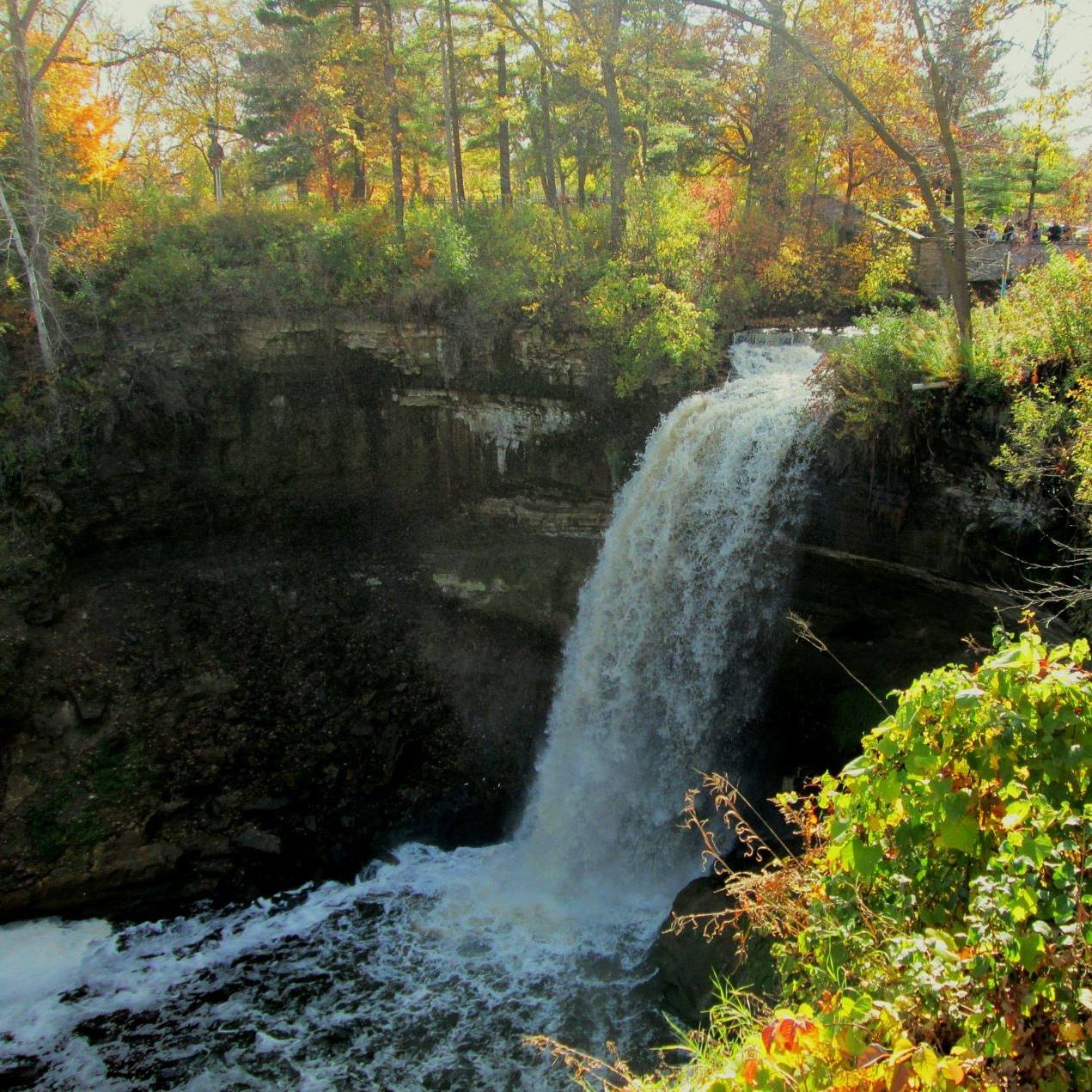 Minnehaha Falls waterfall flowing over dark rock cliff surrounded by autumn trees with colorful leaves