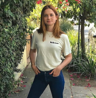 Woman standing on a garden path in a white T-shirt and blue jeans, surrounded by leafy plants