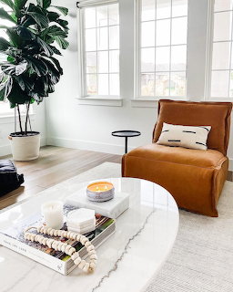 Bright living room with tan velvet chair, marble coffee table, candle, books, and fiddle leaf fig plant