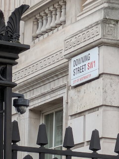 Downing Street SW1 street sign on a stone building behind a black iron fence