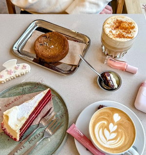 Cafe table with red velvet cake slice, latte art coffee, muffin, spoon, and small sweets