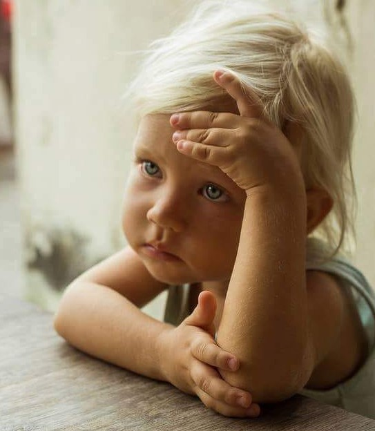Young blonde child with blue eyes resting head on hands while lying down