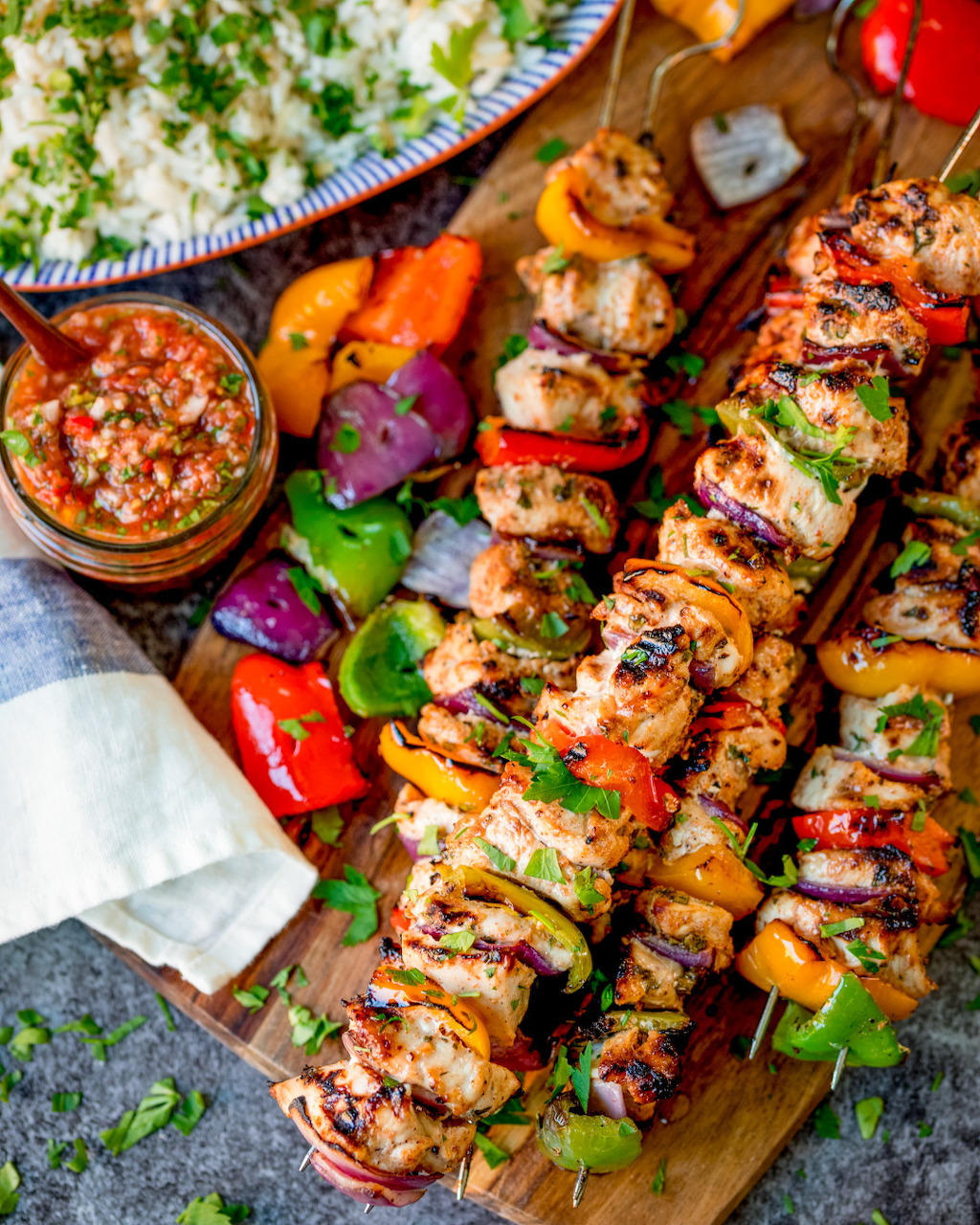 Grilled chicken and vegetable skewers on a wooden cutting board with rice and salsa sauce