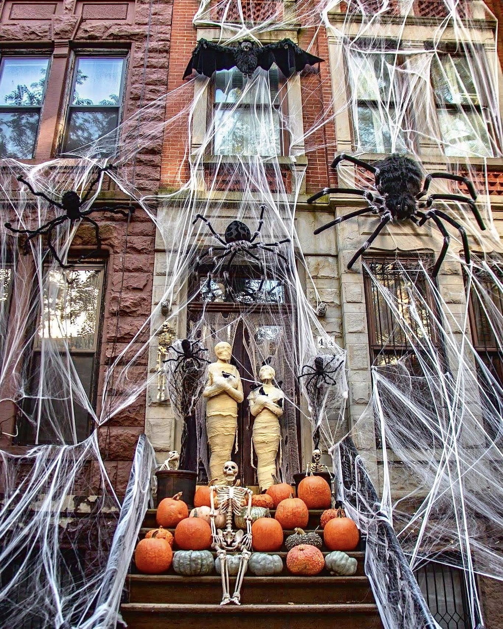 Brick house entrance decorated with Halloween spiderwebs, spiders, skeletons, and pumpkins