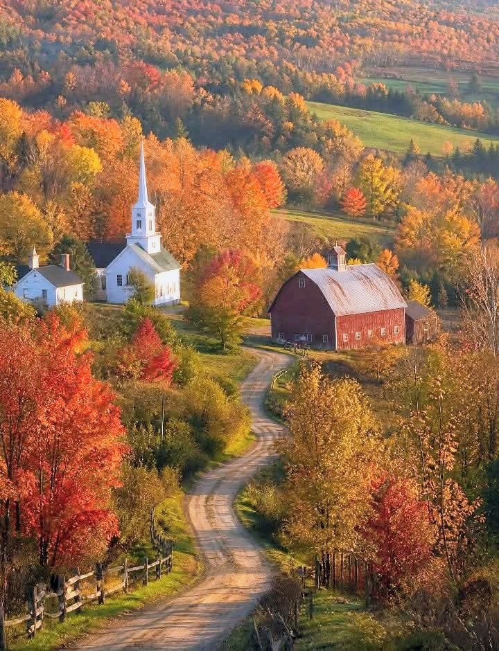 White church and red barn by a winding road among colorful autumn trees