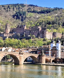 Heidelberg Castle ruins above the stone Old Bridge over the Neckar River, framed by green hills