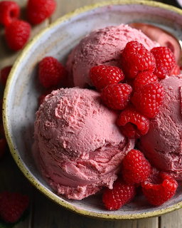 Three scoops of raspberry ice cream with fresh raspberries in a bowl
