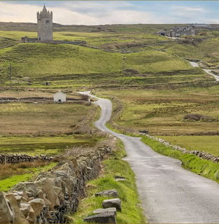 Winding rural road through green fields leading toward Doonagore Castle