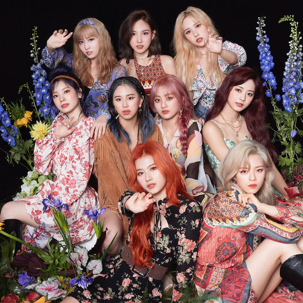 Nine young women in colorful outfits posing together with flowers and elegant lighting in a studio portrait