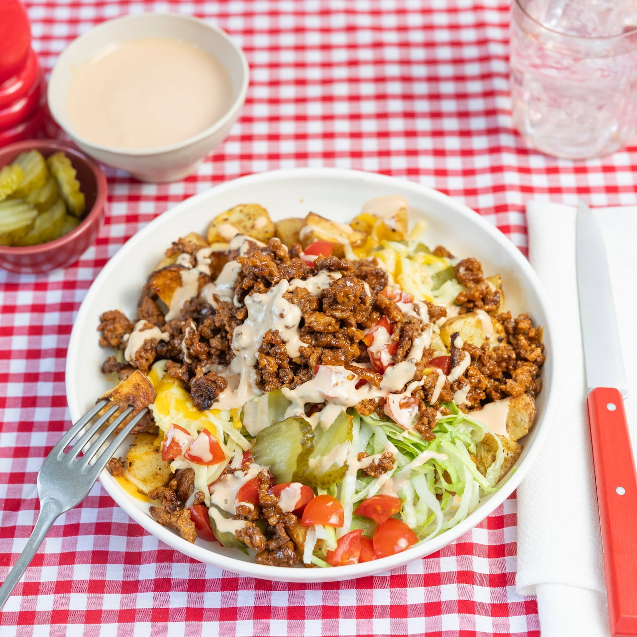 Bowl of taco salad with minced meat, lettuce, tomatoes, cheese, and dressing on a red checkered tablecloth