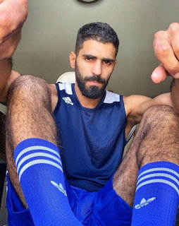 Bearded man wearing blue sports tank top and striped athletic socks flexing arms