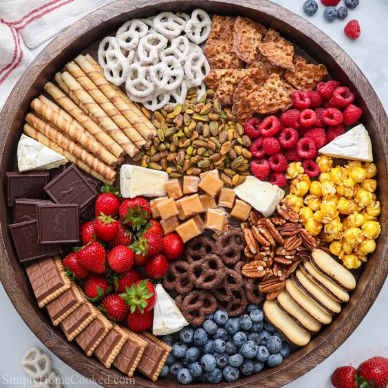 Overhead view of dessert board with chocolate, strawberries, blueberries, cookies, pretzels, and colorful candies