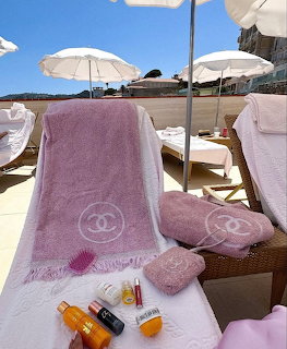 Pink towels on wicker lounge chairs at a beach club with white umbrellas and blue sky