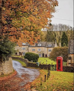 English village lane with stone cottages, red phone box, and autumn trees with orange leaves