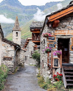 Traditional Alpine village street with stone buildings, church tower, and mountain backdrop