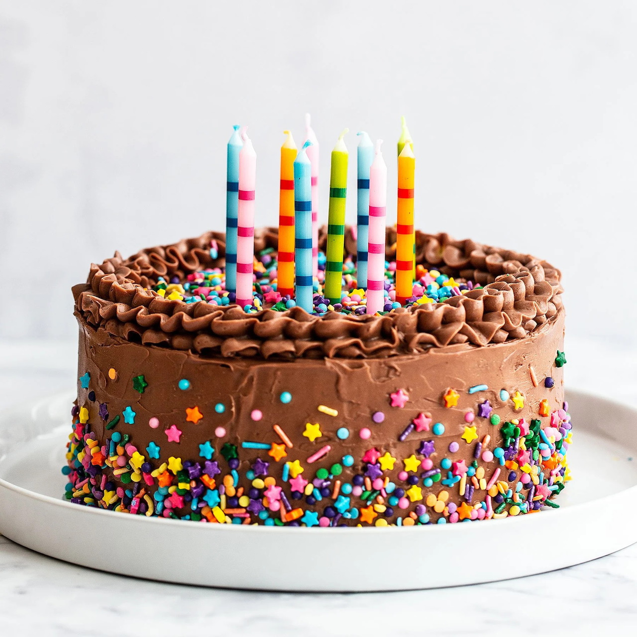 Chocolate birthday cake with rainbow sprinkles and colorful striped candles on white plate