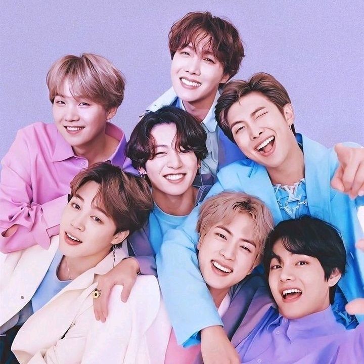 Seven BTS members smiling together in pastel outfits in a studio portrait