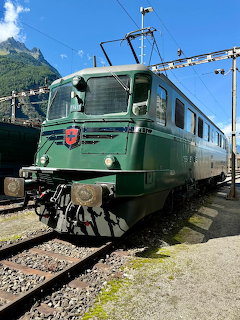 Green SBB Ae 6/6 electric locomotive at a Swiss mountain railway station with overhead catenary wires