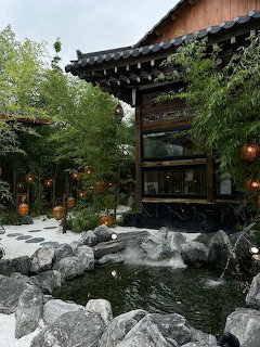 Japanese-style building beside a rock-lined pond with bamboo and garden lanterns