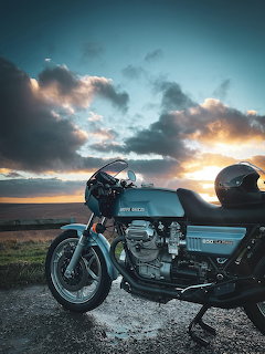 Vintage Moto Guzzi motorcycle silhouetted against colorful sunset sky with dramatic clouds