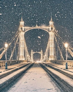 Albert Bridge London lit up at night with snow falling and covering the road