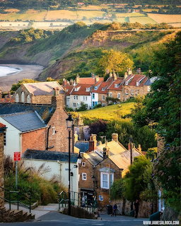 Quaint English coastal village with traditional cottages on hillside overlooking beach and ocean