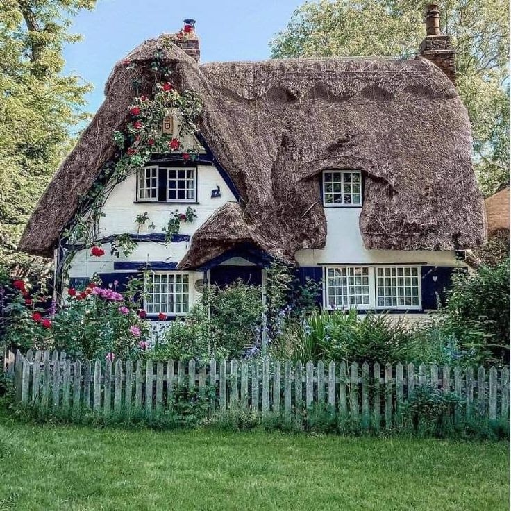 White thatched cottage with garden flowers and picket fence