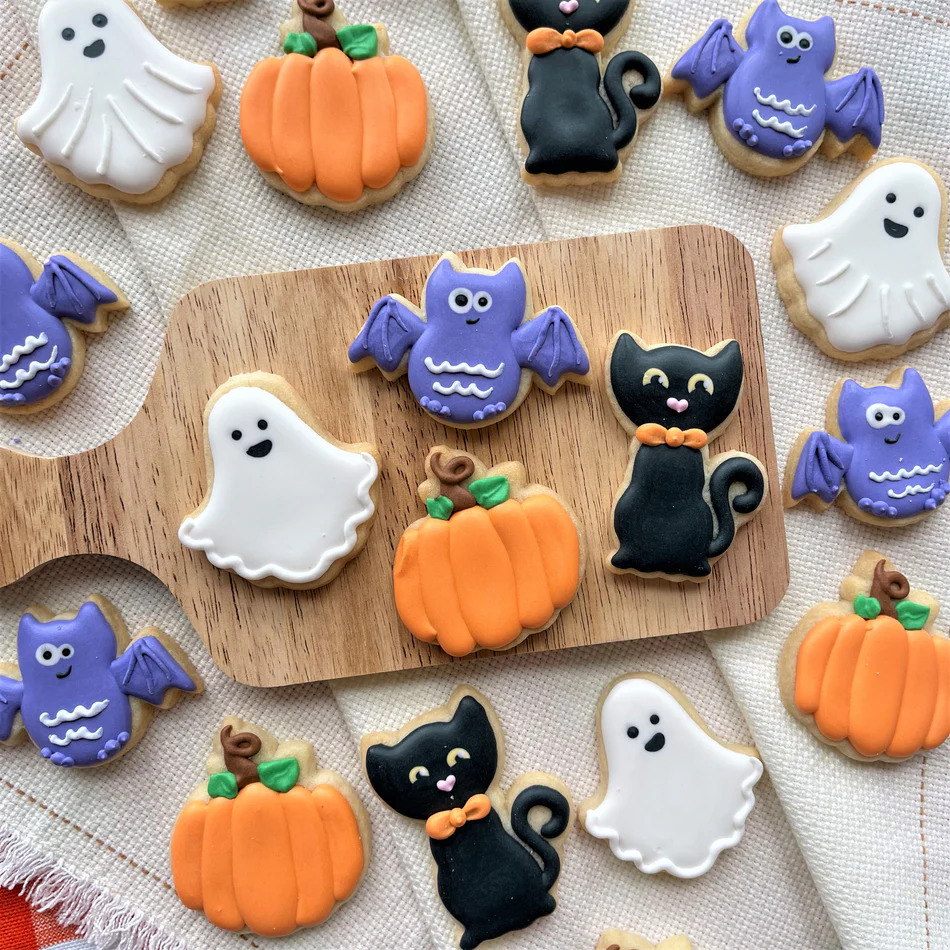 Colorful frosted Halloween cookies with ghosts, pumpkins, cats, and bats on wooden board
