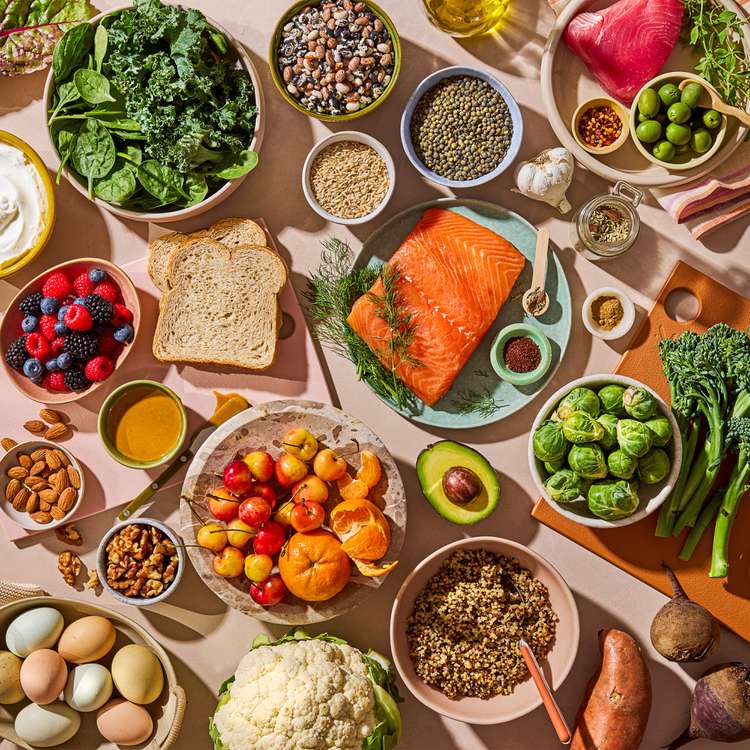 Overhead view of healthy food ingredients including salmon, grens, grains, beries, eggs, and vegetables on a table