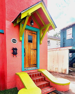 Bright coral pink house exterior with yellow trim, turquoise accents, wooden door, and multi-colored front steps