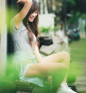 Smiling young woman with long hair sitting on an outdoor step in a gray tank top and white sneakers