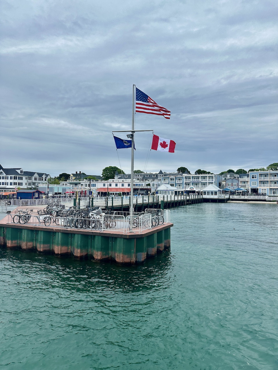 Ferry dock at Mackinac Island with US and Canadian flags, green water and white waterfront buildings behind