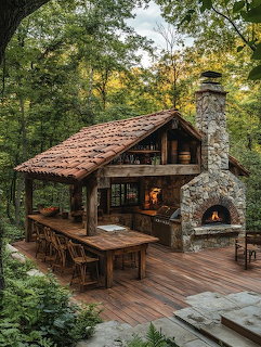 Rustic outdoor kitchen with wooden table, stone fireplace, and forest surroundings