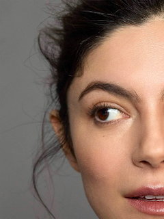 Close-up portrait of Monica Barbaro with dark hair and a gray background