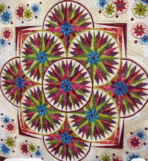 Colorful compasses quilt with radiating star and pinwheel patterns in red, green, blue, and gold on cream fabric