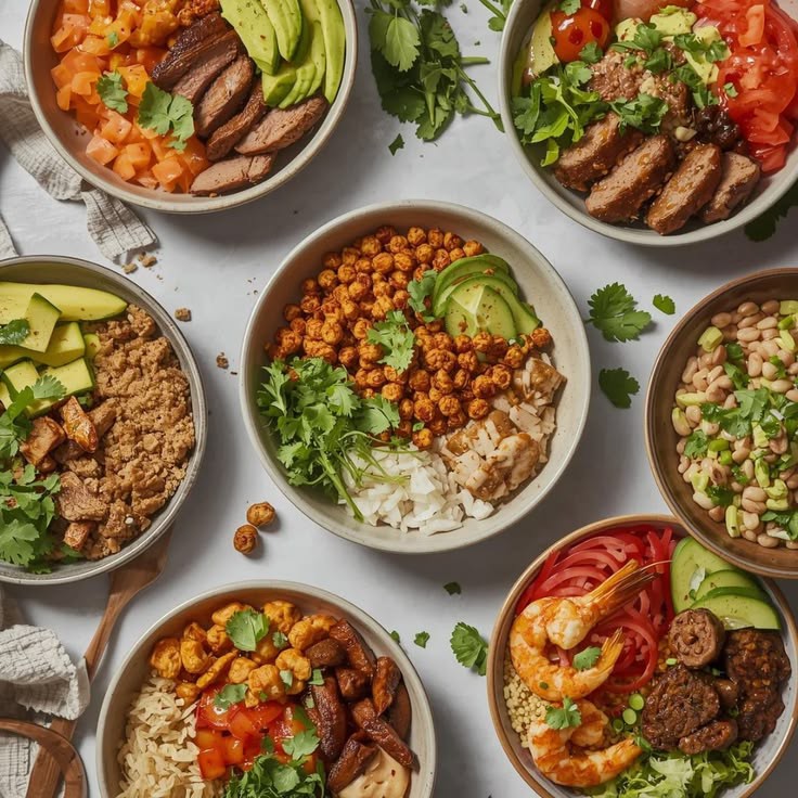 Assorted healthy grain bowls with chicken, vegetables, chickpeas, and avocado on white marble
