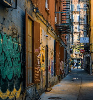 Narrow NYC alley with graffiti walls, fire escapes, and old brick buildings
