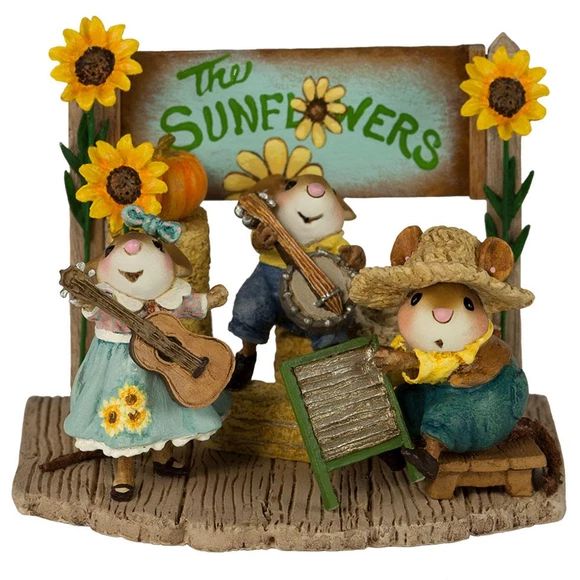 Three decorative mouse figurines wearing hats and dresses, holding guitars, with sunflowers and a rustic sign backdrop