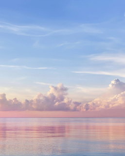Calm ocean at sunset with pastel pink and blue sky and fluffy clouds reflecting on water