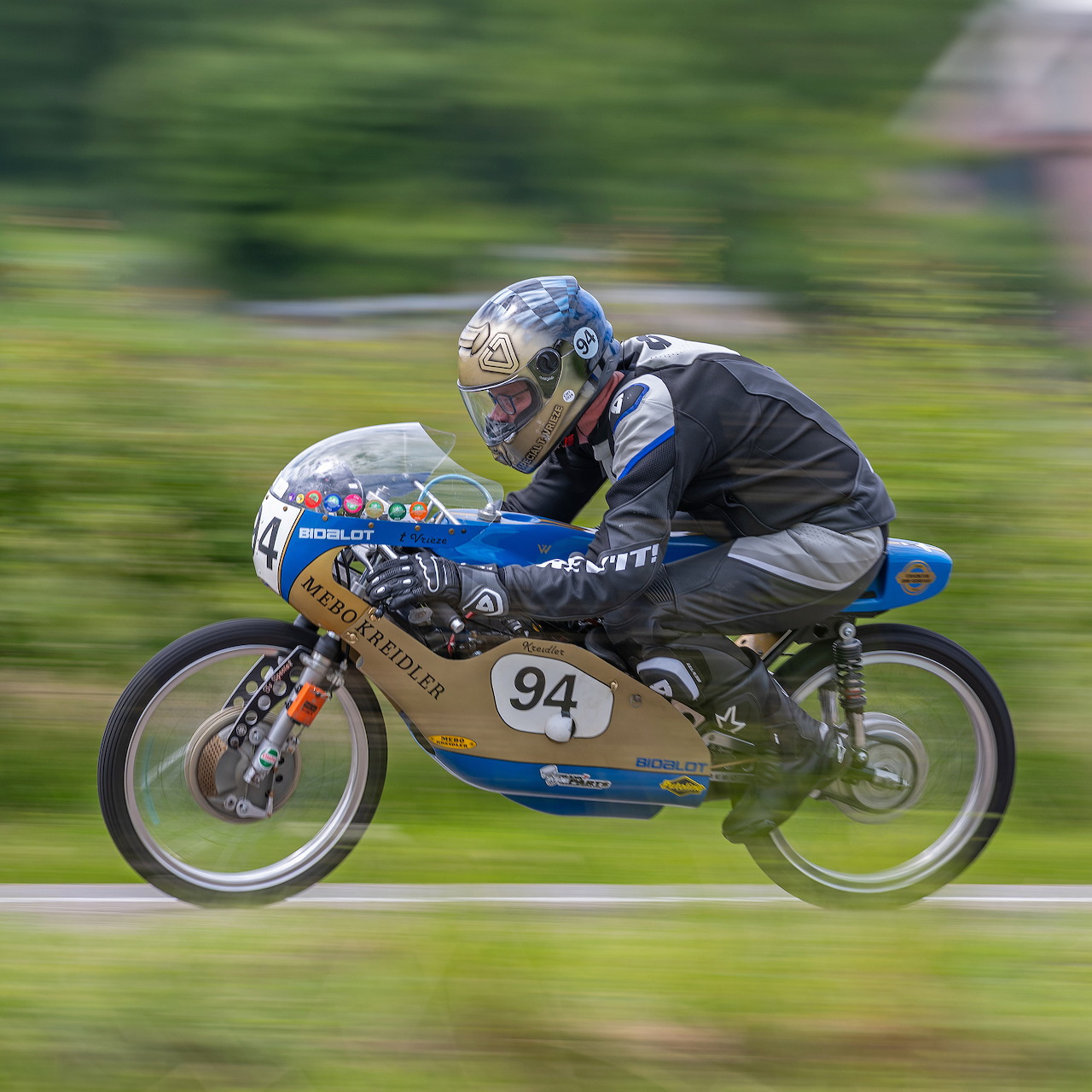 Vintage Kreidler racing motorcycle ridden low on a track with blurred green background