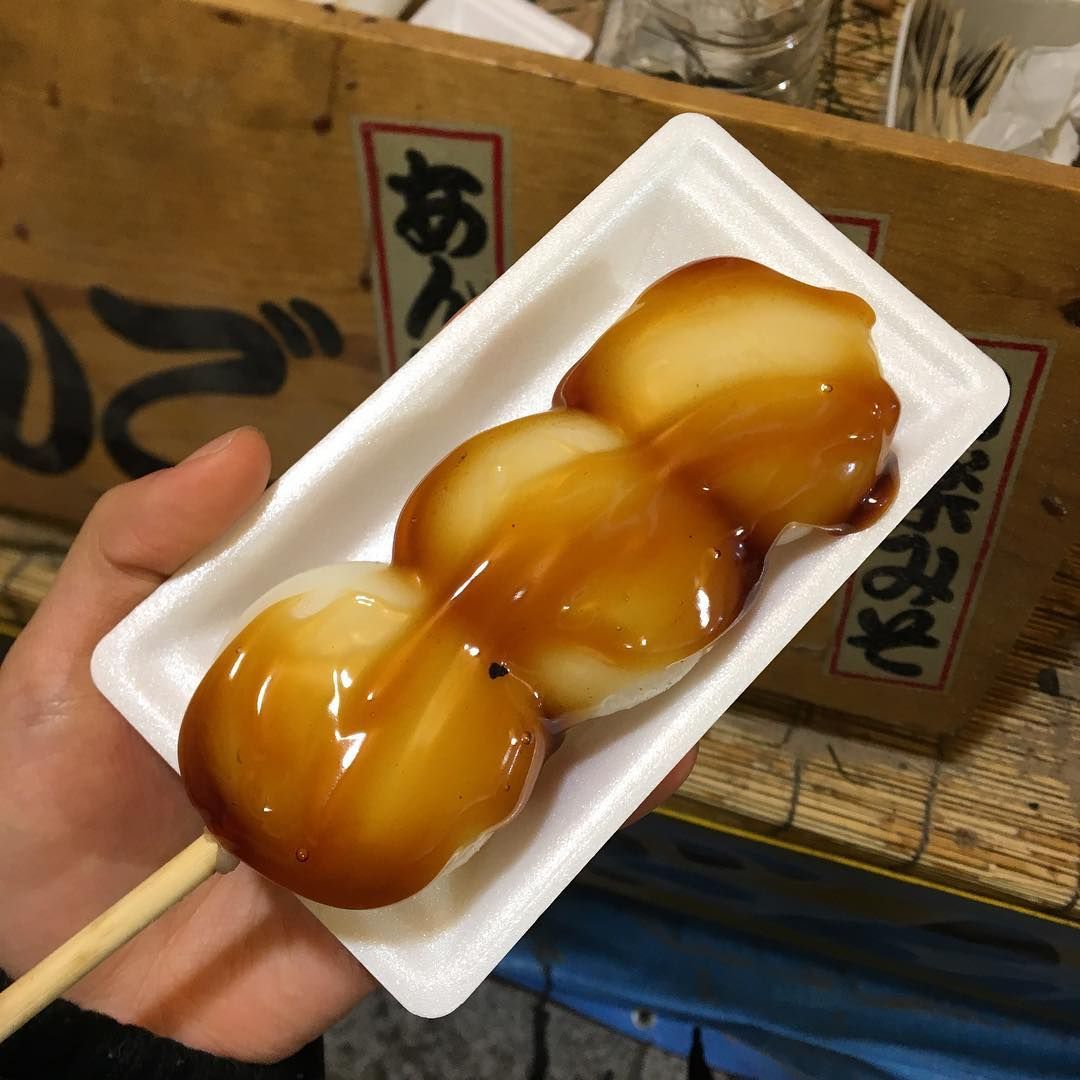 Three glazed mitarashi dango rice dumplings on a skewer in a white tray held by hand