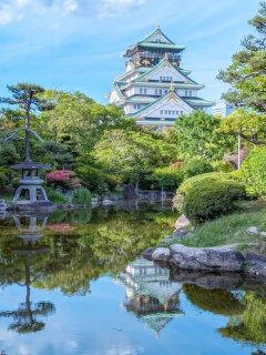 Osaka Castle surrounded by green trees reflected in a tranquil Japanese garden pond
