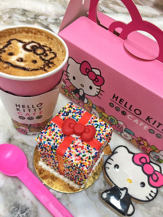 Hello Kity cafe latte with face art, sprinkle dessert, pink box, and Hello Kitty cookie on marble surface