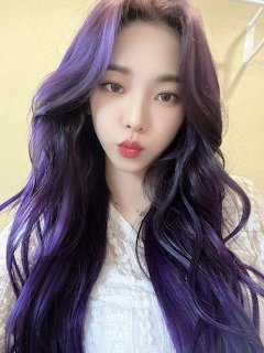 Young Asian woman with long purple and dark wavy hair in a white lace top taking a selfie