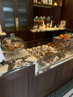 Marble cafe counter with assorted pastries, cookies, and baked goods, wooden shelves in background