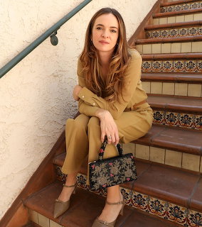 Woman in tan outfit sitting on decorative tiled staircase holding patterned handbag
