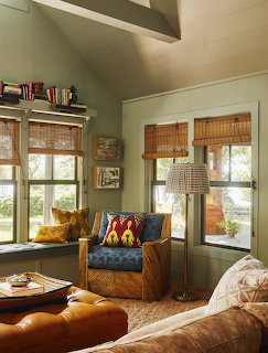 Cozy living room with leather ottoman, wicker armchair, bamboo shades, and sage green walls