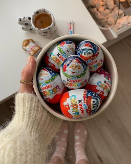 Hand reaching for bowl of assorted Kinder chocolate eggs and treats on table with coffee and cookies
