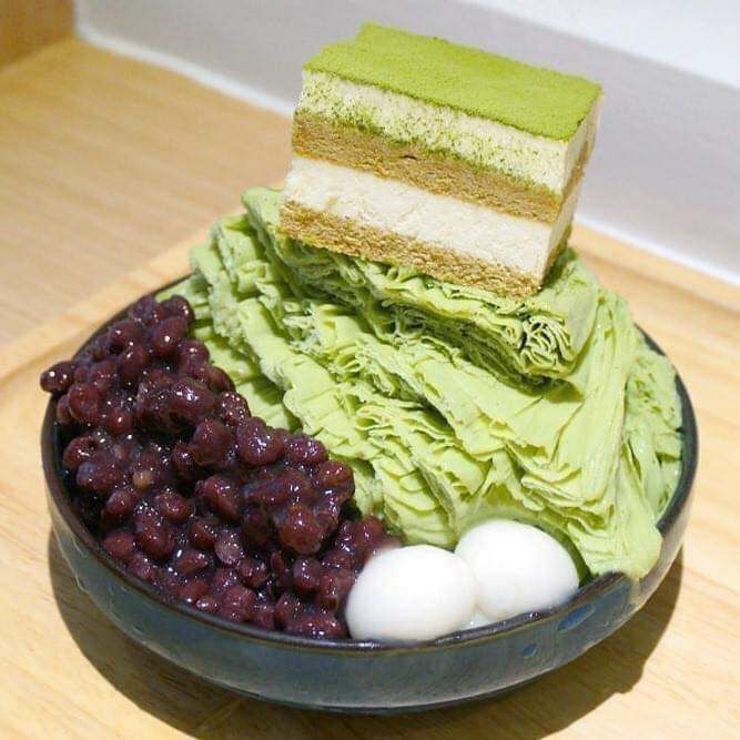 Bowl of green matcha shaved ice with cake, red beans, and mochi