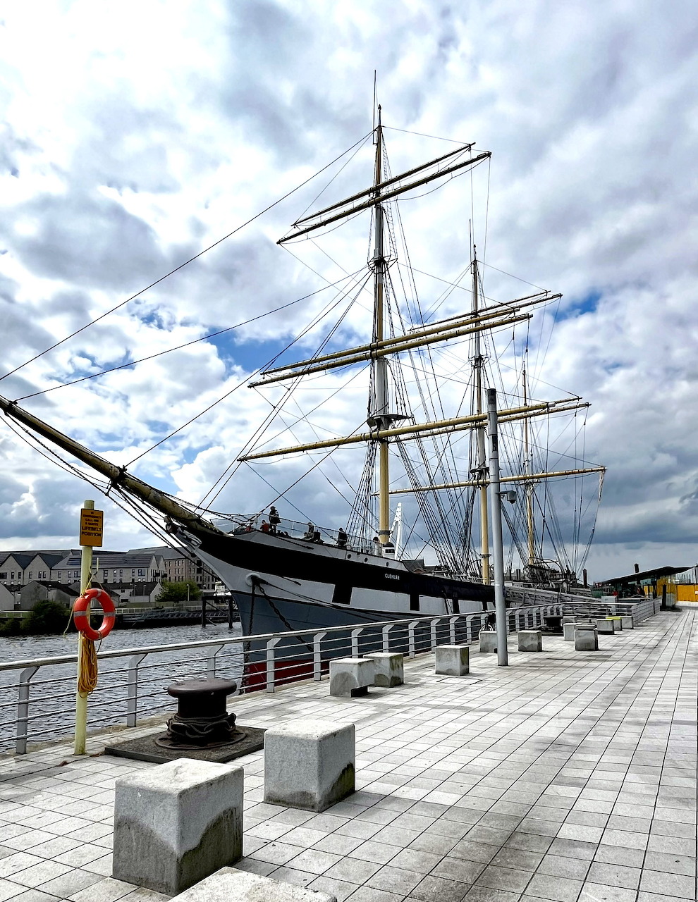 Historic tall ship docked at Glasgow Riverside Museum waterfront under cloudy sky